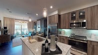 Located at 305 W Commerce St in Dallas, Texas, this single-floor residence showcases a thoughtfully designed open-concept layout that seamlessly blends the kitchen, dining, and living areas into one cohesive space. The kitchen is a standout feature, boasting granite countertops, a generous island with an undermount sink, rich wood-toned cabinetry with glass-front upper panels, stainless steel appliances including a French door refrigerator, electric range, and built-in microwave, all complemented by a soft teal geometric tile backsplash and pendant lighting overhead. The open living and dining area is defined by dark hardwood-style flooring, recessed lighting, and a bold accent wall in deep charcoal that anchors bold decorative artwork. The bedroom offers plush carpeting, a ceiling fan, and large windows that frame outdoor greenery, filling the room with natural light and a sense of calm. The bathroom is finished with light-toned large-format tile flooring, a wood-framed vanity with granite countertop, and a combined tub and shower. Throughout the space, a contemporary design palette of warm wood tones, cool blues, and polished finishes creates a refined and cohesive urban living environment.