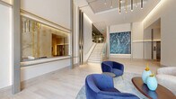 Located at 118 Park Ave in Rutherford, NJ, this sophisticated lobby space delivers a striking first impression through its contemporary architectural design and high-end finishes. Soaring double-height ceilings amplify the sense of openness, while light-toned hardwood flooring extends throughout, lending warmth and continuity to the space. A dramatic large-scale digital display wall serves as a captivating focal point, capable of showcasing vivid, ever-changing imagery. Sleek, illuminated column accents with dark and metallic detailing frame the interior, complementing the refined aesthetic. A built-in reception window, finished with warm stone and brass tones, provides a polished point of service. The lounge area features curved, velvet seating in deep navy and cream tones, arranged atop a soft area rug to create an inviting atmosphere. A sculptural pendant light installation adds a luxurious touch overhead. Floor-to-ceiling marble-paneled walls with integrated LED accent lighting define another seating alcove, elevating the sense of elegance. Large glass entry doors and generous windows allow abundant natural light and views of the surrounding streetscape. A glass-railed staircase and an elevator provide access to upper levels, rounding out this thoughtfully appointed, high-design lobby.