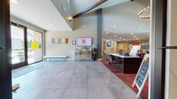 This single-story community clubhouse is designed to serve as a central hub for residents, offering a wide range of amenities within a cohesive, modern layout. The main entrance features large glass doors that flood the tiled entryway with natural light, creating a bright and welcoming first impression. Just inside, the lobby opens into a spacious reception area distinguished by soaring vaulted ceilings with exposed wood beam accents, large-format tile flooring, and a prominent front desk equipped for leasing and resident services. A wall-mounted TV and colorful artwork contribute to the energetic, youthful atmosphere.

Adjacent areas include a well-appointed fitness center with high ceilings, ceiling fans, rubber flooring, and a full array of cardio and strength equipment. A dedicated tanning room provides a private retreat with a full tanning bed. The game room features bar-height seating, a pool cue rack, and a pass-through window. Multiple lounge and common areas offer casual seating arrangements with mounted TVs, accent walls, and café-style tables. A leasing office with floor-to-ceiling windows and vibrant carpet completes the space, reinforcing its student-focused, community-oriented character throughout.