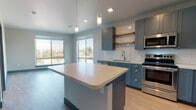 Located at 1648 Eighth Ave in Greeley, Colorado, this single-floor residence showcases a thoughtfully designed, contemporary interior with a cohesive color palette of slate blue, soft gray, and crisp white carried throughout every room. The open-concept kitchen serves as the heart of the home, featuring blue-gray shaker cabinetry, a white subway tile backsplash, light quartz countertops, and a central island with pendant lighting overhead. A full suite of stainless steel appliances—including a refrigerator, range, microwave, and dishwasher—completes the space, while large windows invite abundant natural light and outdoor views. Light wood-look flooring flows seamlessly throughout the unit, complemented by bold teal baseboards that add a distinctive design accent. The bedrooms are generously proportioned, each benefiting from natural light and notable architectural details such as sliding barn-style doors in teal, providing both style and functionality. Walk-in closet access is featured in at least one bedroom. Two bathrooms mirror the kitchen's design language, offering blue-gray vanity cabinetry, quartz countertops, framed mirrors, and light wood flooring. One bathroom includes a tiled walk-in shower with grab bars, while the other features a full vanity with ample drawer storage. The overall ambiance is clean, modern, and move-in ready.