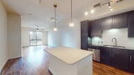 This single-floor residence offers a thoughtfully designed open-concept layout with rich hardwood flooring throughout the main living areas. The kitchen serves as a central hub, featuring dark espresso cabinetry that extends to the ceiling, a white quartz island with pendant lighting overhead, a subway tile backsplash, and a full suite of stainless steel appliances including a refrigerator, range, microwave, and dishwasher. Track lighting supplements the space with focused illumination. The open living area flows seamlessly from the kitchen, bathed in natural light from a sliding glass door that opens to a balcony offering views of the surrounding urban skyline. A ceiling fan adds comfort to the space. The bedrooms are carpeted and generously proportioned, each featuring ceiling fans and sliding glass doors to private balconies with city views, including a notable architectural landmark visible from one bedroom. The primary bathroom is equipped with a dual-sink vanity topped with granite countertops, a large wall mirror, and tile flooring. A secondary bathroom mirrors this design with granite countertops, a single-sink vanity, and tile flooring.