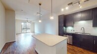 This single-floor residence offers a thoughtfully designed open-concept layout with rich hardwood flooring throughout the main living areas. The kitchen serves as a central hub, featuring dark espresso cabinetry that extends to the ceiling, a white quartz island with pendant lighting overhead, a subway tile backsplash, and a full suite of stainless steel appliances including a refrigerator, range, microwave, and dishwasher. Track lighting supplements the space with focused illumination. The open living area flows seamlessly from the kitchen, bathed in natural light from a sliding glass door that opens to a balcony offering views of the surrounding urban skyline. A ceiling fan adds comfort to the space. The bedrooms are carpeted and generously proportioned, each featuring ceiling fans and sliding glass doors to private balconies with city views, including a notable architectural landmark visible from one bedroom. The primary bathroom is equipped with a dual-sink vanity topped with granite countertops, a large wall mirror, and tile flooring. A secondary bathroom mirrors this design with granite countertops, a single-sink vanity, and tile flooring.