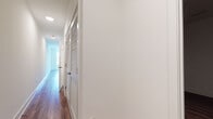 This well-appointed single-floor unit offers a clean, contemporary design with a cohesive aesthetic carried throughout every room. The open-concept kitchen is a standout feature, outfitted with dark espresso cabinetry, white quartz countertops, a white subway tile backsplash, and a full suite of stainless steel appliances including a gas range, microwave, dishwasher, and refrigerator. Track lighting overhead and multiple windows allow natural light to fill the space, with views of surrounding greenery adding a sense of openness.

Warm hardwood-style flooring extends through the main living areas, kitchen, and bedrooms, providing a unified and inviting feel. The bedrooms are generously sized with clean white walls, large windows fitted with blinds, and ample closet space — including a walk-in closet with built-in hanging rods in at least one bedroom.

The bathroom is finished in a modern style, featuring a soaking tub and shower combination with white tile surround, a dark wood vanity with white countertop, an integrated sink, and a backlit mirror that adds a refined, contemporary touch. Light tile flooring completes the look.

A well-proportioned hallway connects the rooms, featuring louvered closet doors for additional storage. The overall design emphasizes functionality, clean lines, and bright, neutral tones throughout.