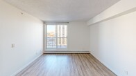 Located at 10904 102nd Ave NW in Edmonton, Alberta, this well-appointed one-bedroom, one-bathroom unit offers a smart and functional layout across a single floor. The open-concept living, dining, and kitchen area forms the heart of the space, creating a seamless flow ideal for everyday living and entertaining. The kitchen features white cabinetry, dark countertops, tile flooring, and white appliances, all illuminated by a sleek track lighting system. A peninsula counter separates the kitchen from the living and dining area, which transitions into warm hardwood-style flooring and offers views of the surrounding Edmonton skyline through large windows. The spacious bedroom includes a walk-in closet with built-in shelving and a large window that fills the room with natural light and urban views. A versatile den provides additional flexible space suitable for a home office or guest room. Three closets throughout the unit offer generous storage. The full bathroom features tile flooring, a wide vanity with dark countertop, and a tub-shower combination. In-unit laundry adds everyday convenience. The clean, neutral palette and consistent finishes throughout lend the space a bright, cohesive, and move-in ready ambiance.