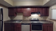 Located at 2233 Courtside Dr in Columbus, Ohio, this single-floor unit offers a practical and functional layout across several distinct living areas. The floor plan, as seen in the 3D overview, presents a well-organized arrangement of living, sleeping, kitchen, and bathroom spaces.

The kitchen is a standout feature, equipped with rich dark cherry wood cabinetry extending to the upper walls, providing generous storage throughout. Dark laminate countertops run the length of the workspace, complemented by stainless steel appliances including an electric range, dishwasher, and refrigerator. An under-cabinet range hood and a single-basin sink complete the setup. The kitchen opens via a breakfast bar peninsula into the main living area.

The living room is a generously sized, carpeted space featuring neutral-toned walls, a textured ceiling, and a window that brings in natural light and outdoor views. A wall-mounted air conditioning unit and baseboard heating provide year-round climate control.

The bedrooms are carpeted and finished with neutral walls and textured ceilings. Each room features windows with blinds, baseboard heating, and a wall A/C unit. One bedroom includes a double closet with sliding doors for added storage.

The bathroom is cleanly finished with wood-look flooring, a white tub/shower surround, a toilet, and a vanity with an integrated sink and mirror.