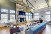 Located at 16789 Chandler Rd in East Lansing, Michigan, this expansive single-story community amenity center offers a diverse range of facilities designed to support recreation, fitness, productivity, and relaxation. The standout feature of the space is its dramatic vaulted great room, where soaring ceilings are accented by striking exposed beam trusses, ceiling fans, and an abundance of natural light streaming through large multi-pane windows. This open area serves as a central hub, housing a ping-pong table, a full-size pool table with pendant lighting, and comfortable lounge seating arranged on area rugs over warm hardwood flooring — all finished in a calming palette of soft blues and whites. Adjacent to the game and lounge area is a well-equipped fitness center featuring treadmills, cable machines, free weights, and cardio equipment laid out across a rubber-floored workout space with ceiling fans and ample overhead lighting. A dedicated business center provides residents with workstations, computers, and printing equipment set against acoustically treated walls. A welcoming reception waiting area with cushioned seating connects to private rooms, including a tanning room adorned with warm string lights for a relaxing ambiance. Throughout, the space maintains a cohesive, community-focused design ideal for active and social lifestyles.