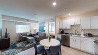 Located at 1012 Shiloh Way in Morrisville, NC, this single-floor suite offers a thoughtfully designed layout that balances comfort and functionality. The open-concept living and dining area serves as the heart of the space, featuring light wood-style flooring, recessed lighting, and large windows fitted with horizontal blinds that allow for ample natural light. The living area is furnished with a plush sofa, accent chairs, and a mint-green ottoman, complemented by vibrant teal abstract artwork that sets a cohesive color palette throughout.

The full kitchen is equipped with stainless steel appliances — including a range, microwave, refrigerator, and dishwasher — alongside white cabinetry, granite countertops, and a double sink, making it well-suited for extended stays or everyday cooking.

Two bedrooms each feature a king-sized bed, dedicated storage cabinetry, nightstands, and matching teal wall art. One bedroom includes an en-suite bathroom with a glass-enclosed shower, while the other connects to a full bathroom with a shower-tub combination. A stacked washer and dryer unit is conveniently integrated into the bathroom area, adding a practical amenity for longer-term occupants. The overall aesthetic is clean, modern, and inviting throughout.