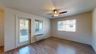 This single-story unit on Matzen Street in Saint Helens, Oregon, offers a well-designed layout with consistent wood-look flooring flowing throughout the living areas and bedrooms. The living room serves as a welcoming central space, featuring a ceiling fan with integrated lighting, a wall-mounted HVAC unit, and multiple windows that bring in generous natural light. A glass exterior door provides direct outdoor access and adds to the bright, open feel of the room.

The kitchen is designed for functionality, featuring a galley-style layout with warm wood cabinetry, granite-style countertops, an undermount sink, and a full suite of black appliances including a refrigerator, electric range, microwave, and dishwasher. Upper and lower cabinets provide ample storage, and the space connects conveniently to additional storage and the rest of the unit.

The bedrooms continue the wood-look flooring and are naturally lit by well-placed windows with blinds. Each room includes ceiling fans and wall heating units for comfort year-round.

Two bathrooms serve the unit, each finished with warm wood vanities, granite-style countertops, and light tile flooring. One bathroom features a soaking tub and shower combination, while the other includes a walk-in shower, offering practical flexibility for residents.