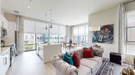 This single-floor residence is defined by a thoughtfully designed open-concept layout that seamlessly connects the main living areas. The kitchen is outfitted with white cabinetry, quartz countertops, a tile backsplash, stainless steel appliances, and a peninsula with a undermount sink, all illuminated by pendant lighting and large windows offering urban views. Adjacent to the kitchen, the dining area benefits from expansive floor-to-ceiling windows with roller shades, flooding the space with natural light and framing city views. The living room features light wood-style flooring, a ceiling fan, and ample space for comfortable seating arrangements. The bedroom includes a ceiling fan, a window with exterior views, and direct access to a well-appointed bathroom and a spacious walk-in closet with built-in wire shelving. The bathroom is finished with light wood-style flooring, a clean-lined vanity with white cabinetry and brushed nickel hardware. Throughout, neutral tones, light flooring, and modern fixtures create a cohesive, contemporary aesthetic suited to urban living.
