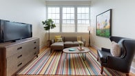 This single-floor unit at 523 West Street in Bristol, Connecticut offers a well-organized layout that makes efficient use of its compact footprint. Warm hardwood flooring flows throughout the space, providing a cohesive and inviting atmosphere across all rooms.

The living area serves as the central gathering space, anchored by large multi-pane windows that flood the room with natural light. The bright, neutral walls complement the vibrant striped area rug and eclectic wall art, creating an energetic yet comfortable ambiance. A mix of seating, including a gray sectional sofa and a dark leather accent chair, provides ample space for relaxation.

The kitchen features soft blue-gray cabinetry paired with granite-look countertops and stainless steel appliances, including a dishwasher, electric range, and over-range microwave. The hardwood floors continue here, adding warmth to the functional cooking space.

The bedroom is a calm, well-lit retreat with large windows allowing generous natural light. Light neutral walls and hardwood floors create a serene environment, with room for a dresser and additional furnishings.

The full bathroom is finished with large-format tile flooring, a white vanity with a medicine cabinet mirror, and a full soaking tub with shower, offering a clean and functional design.