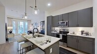 This contemporary 1-bedroom, 1-bathroom residence offers a well-designed layout that maximizes functionality and style across a single floor. The open-concept kitchen is a standout feature, showcasing slate-grey cabinetry extending to the ceiling, a white subway tile backsplash, stainless steel appliances including a refrigerator, electric range, and built-in microwave, and a central island with a white quartz countertop that seats multiple guests beneath elegant globe pendant lights. The kitchen flows seamlessly into the living room, which is bathed in natural light from large floor-to-ceiling windows and a glass-paneled door opening to a balcony. A ceiling fan adds comfort, and light wood-style flooring runs throughout the common areas, enhancing the bright, airy atmosphere. The bedroom is a serene retreat with its own access to natural light through expansive windows, a ceiling fan, and ample space for a full furniture arrangement. The bathroom features a clean, all-white design with a grey floating vanity, a walk-in shower enclosed by black-framed glass doors, and marble-style tile walls and flooring. A dedicated closet completes the thoughtfully organized layout of this modern residence.