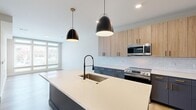 Located on North Arthur Ashe Boulevard in Richmond, Virginia, this contemporary one-bedroom, one-bathroom residence offers a well-designed open-concept layout with modern finishes throughout. The kitchen is a standout centerpiece, featuring a large island with a white quartz countertop, an undermount sink with a matte black faucet, two-tone cabinetry combining slate-blue lower cabinets with warm wood-toned uppers, a white subway tile backsplash, stainless steel appliances, and striking black pendant lights. Light hardwood flooring flows seamlessly through the kitchen and living areas, enhancing the bright, airy atmosphere. The living room offers ample natural light and a clean, neutral palette. The bedroom is carpeted for comfort and includes a ceiling fan, generous closet access, and large windows with horizontal blinds that frame views of the surrounding Richmond cityscape. The bathroom is thoughtfully appointed with a navy shaker-style vanity with gold hardware, white quartz countertops, a tub-shower combo with subway tile surround, and a bold dark-painted door with matte black fixtures, adding a sophisticated contrast to the light walls and hardwood flooring throughout.