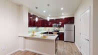 This single-floor residence offers a thoughtfully designed layout that balances style and functionality throughout. The centerpiece of the space is a striking kitchen, featuring deep mahogany-toned cabinetry with polished nickel hardware, crisp white countertops, and a green glass tile mosaic backsplash. Stainless steel appliances, including a refrigerator, range, and microwave, complement the kitchen's modern aesthetic, while pendant lighting and recessed fixtures illuminate the space with warm, inviting light. A peninsula counter with seating provides a natural transition into the open living and dining area, which is finished with durable wood-look plank flooring and neutral-toned walls.

The bedrooms are carpeted for comfort and feature large windows that allow generous natural light and views of the surrounding greenery. Each room provides a calm, versatile space with clean lines and neutral finishes.

Two full bathrooms serve the residence, each appointed with white vanities, tub-shower combinations, and wood-look flooring. One bathroom features built-in open shelving for added storage and a decorative shower curtain, while the other offers a large wall mirror and straightforward, clean fixtures. Together, the rooms create a cohesive, move-in-ready living environment with a modern yet comfortable character.