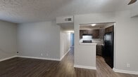This single-floor unit offers a practical and cohesive layout connecting the living areas, kitchen, and bedrooms through a straightforward open-concept design. The living and dining areas feature dark hardwood-style flooring paired with neutral gray walls and textured ceilings, creating a clean and understated aesthetic. Natural light enters through blinds-fitted windows, contributing to a bright atmosphere throughout. A half-wall partition separates the living space from the galley-style kitchen, which is outfitted with dark espresso cabinetry, granite-look countertops, and black appliances including a range and refrigerator. The kitchen also features matching hardwood-style flooring, maintaining continuity with the main living area. The bedrooms are carpeted and finished with the same neutral gray palette, each featuring windows that allow natural light and closets with bi-fold doors for storage. The bathroom includes a full-size soaking tub with an overhead shower, white surround walls, and standard fixtures. Textured ceilings are consistent throughout the unit, and white baseboards provide a clean contrast against the flooring in every room.