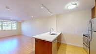 Located at 1935 Addison St in the heart of Berkeley, CA, this two-bedroom, one-bathroom residence offers a well-designed single-floor layout. The open-concept kitchen and living area serves as the centerpiece of the home, featuring a sleek kitchen island with a white quartz countertop, an undermount sink, warm wood cabinetry, and stainless steel appliances including a refrigerator, range, and dishwasher. Track lighting overhead and recessed fixtures illuminate the space, while light bamboo hardwood flooring extends throughout the living and kitchen areas, adding warmth and continuity. The spacious primary bedroom is carpeted for comfort and is generously sized, while the second bedroom benefits from large windows that invite abundant natural light and offer views of the surrounding Berkeley neighborhood. Both bedrooms feature soft neutral tones and individual climate controls. The bathroom is clean and modern, outfitted with large-format tile flooring, a combination tub and shower with mosaic tile accent detailing, and a wood-accented vanity with a white countertop. The overall design is cohesive and contemporary, with warm cream-toned walls and functional finishes throughout.
