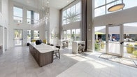 This sophisticated single-floor amenity space is defined by its striking architectural design, most notably the soaring double-height ceilings and expansive floor-to-ceiling windows that flood the interior with natural light and offer sweeping views of the surrounding outdoor pool and palm-lined landscape. The open-plan layout creates a seamless flow between distinct functional zones, each thoughtfully appointed for both relaxation and social interaction.

The main lounge and gathering area centers around a large marble-topped island with bar seating beneath a cluster of globe pendant lights, complemented by a built-in kitchenette featuring dark wood cabinetry, dual wall-mounted televisions, a microwave, and a sink — ideal for hosting events. Generous windows and glass doors open the space to the outdoors, blurring the line between interior comfort and alfresco living.

A dedicated game room provides entertainment with a full-size billiards table, foosball, a wall-mounted flat-screen TV, and casual seating set against a bold golden-yellow accent wall. A cozy nook with a round dining table, chartreuse tufted seating, and woven wall art offers intimate conversation or casual dining with pool views. Throughout, the palette of crisp whites, warm yellows, and natural textures creates a welcoming, contemporary ambiance.