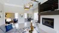 Located at 1910 Capital Creek Drive in Wake Forest, NC, this single-floor space showcases a refined, contemporary design that balances comfort and sophistication. The open-plan layout allows for seamless flow between the main lounge and an adjacent dining or gathering area, creating a welcoming environment for residents and guests alike.

The main lounge is anchored by a striking dark-paneled fireplace wall, which provides a bold focal point and a cozy ambiance. Above the seating area, a pair of large, mercury-glass globe pendant lights serve as eye-catching statement pieces, casting a warm glow throughout the room. The light palette of white and soft gray walls, combined with polished tile flooring, amplifies the sense of openness and brightness.

Multiple large windows invite abundant natural light throughout the day, enhancing the airy atmosphere. The interior is thoughtfully appointed with modern furnishings, including plush seating, a geometric patterned area rug in navy and white, and carefully selected accent pieces that add depth and character to the space.

An adjoining room, visible through a wide opening, offers additional seating and dining options, with large windows framing views of the surrounding area. Together, these spaces offer a polished, well-designed environment that is both functional and visually impressive.