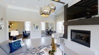 Located at 1910 Capital Creek Drive in Wake Forest, NC, this single-floor space showcases a refined, contemporary design that balances comfort and sophistication. The open-plan layout allows for seamless flow between the main lounge and an adjacent dining or gathering area, creating a welcoming environment for residents and guests alike.

The main lounge is anchored by a striking dark-paneled fireplace wall, which provides a bold focal point and a cozy ambiance. Above the seating area, a pair of large, mercury-glass globe pendant lights serve as eye-catching statement pieces, casting a warm glow throughout the room. The light palette of white and soft gray walls, combined with polished tile flooring, amplifies the sense of openness and brightness.

Multiple large windows invite abundant natural light throughout the day, enhancing the airy atmosphere. The interior is thoughtfully appointed with modern furnishings, including plush seating, a geometric patterned area rug in navy and white, and carefully selected accent pieces that add depth and character to the space.

An adjoining room, visible through a wide opening, offers additional seating and dining options, with large windows framing views of the surrounding area. Together, these spaces offer a polished, well-designed environment that is both functional and visually impressive.