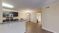 Located at 212 Katherine Blvd in Palm Harbor, Florida, this single-floor residence offers a well-designed open-concept layout that seamlessly connects the kitchen, dining, and living areas. The kitchen is a standout feature, showcasing rich dark cabinetry, granite countertops, and a full suite of stainless steel appliances including a refrigerator, electric range, and built-in microwave. A peninsula with bar-style seating and an elegant pendant light above adds both functionality and style to the space. Crown molding accents the main living areas, and durable wood-look flooring runs throughout the kitchen and living spaces, lending a clean, modern aesthetic. The bathroom is well-appointed with a granite-topped dark vanity, a full tub-shower combination with tiled surround, and coordinating wood-look flooring. The bedrooms feature plush carpeting for added comfort, with one room offering a ceiling fan with light fixture and a window with vertical blinds for natural light control. Closet storage is available throughout, including bi-fold door closets visible in the main living area. The overall ambiance is bright, neutral, and move-in ready, reflecting a practical yet polished interior well-suited to the sunny Palm Harbor lifestyle.