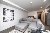 Located at 610 E Walnut St in Des Moines, Iowa, this efficiently designed single-floor unit offers a thoughtfully laid-out living experience with a clean, contemporary aesthetic. The open-plan kitchen and living area serves as the heart of the space, where rich, dark-toned cabinetry contrasts beautifully with white quartz countertops and a light tile backsplash. A full suite of stainless steel appliances — including a refrigerator, range, over-the-range microwave, and dishwasher — equips the kitchen for everyday functionality. The living area flows naturally from the kitchen, featuring light wood-look flooring that runs throughout, recessed lighting, and a window with roller shades that invites natural light. The hallway connects the main living space to the bathroom and additional rooms, maintaining a clean and organized layout. The bathroom is well-appointed with dark cabinetry, a white vanity countertop, a large framed mirror, and a shower-tub combo, all finished with the same wood-look tile flooring for visual continuity. Crisp white walls and recessed lighting throughout lend the space a bright, modern character well-suited to urban living in downtown Des Moines.