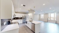 Located at 119 E Sixth St in the heart of downtown Tulsa, Oklahoma, this thoughtfully designed 2-bedroom, 2-bathroom residence offers a seamless blend of modern aesthetics and functional living. The open-concept kitchen and living area serves as the centerpiece of the home, featuring white shaker cabinetry, quartz countertops, a bold geometric tile backsplash, stainless steel appliances, and a large center island with a undermount sink — all illuminated by stylish gold pendant lighting and recessed fixtures. Tray ceilings add architectural depth throughout, while durable wood-look flooring flows through the main living areas. The spacious living room benefits from natural light through large windows and offers generous room for a variety of furniture arrangements. The primary bedroom is notably expansive, finished with plush patterned carpet, a ceiling fan, a tray ceiling, and direct access to a private bathroom. The well-appointed bathrooms feature white vanities with quartz countertops, matte black hardware, large mirrors, and marble-look tile flooring. A dedicated laundry area with in-unit washer adds everyday convenience. A hallway and closet provide additional storage, completing this well-organized and refined urban residence.