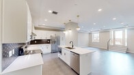 Located at 119 E Sixth St in the heart of downtown Tulsa, Oklahoma, this thoughtfully designed 2-bedroom, 2-bathroom residence offers a seamless blend of modern aesthetics and functional living. The open-concept kitchen and living area serves as the centerpiece of the home, featuring white shaker cabinetry, quartz countertops, a bold geometric tile backsplash, stainless steel appliances, and a large center island with a undermount sink — all illuminated by stylish gold pendant lighting and recessed fixtures. Tray ceilings add architectural depth throughout, while durable wood-look flooring flows through the main living areas. The spacious living room benefits from natural light through large windows and offers generous room for a variety of furniture arrangements. The primary bedroom is notably expansive, finished with plush patterned carpet, a ceiling fan, a tray ceiling, and direct access to a private bathroom. The well-appointed bathrooms feature white vanities with quartz countertops, matte black hardware, large mirrors, and marble-look tile flooring. A dedicated laundry area with in-unit washer adds everyday convenience. A hallway and closet provide additional storage, completing this well-organized and refined urban residence.