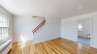 Located at 112 Kendall Ct in Dover, NJ, this two-story unit offers a well-organized layout across two distinct floors. The main level, which comprises the larger portion of the space, houses the living room and kitchen. The living room is a bright, open area featuring polished hardwood floors, white walls, and a large multi-pane window that allows natural light to fill the room. A classic wood-railed staircase leads to the upper level, adding architectural character. An entry door with sidelights provides direct access from the exterior.

The kitchen is equipped with warm honey-toned wood cabinetry — both upper and lower — offering ample storage. White appliances, including a freestanding range and a full-size refrigerator, are included. A single-basin sink sits beneath a window, and light-toned vinyl tile flooring completes the space.

Upstairs, the bedroom is a well-proportioned room with hardwood floors, crisp white walls, crown molding, and two windows that bring in natural light. The full bathroom features a tiled tub-shower combination, a white vanity with sink, a medicine cabinet mirror, and classic patterned tile flooring. A hallway connects the upper-level rooms, completing this practical and cohesive two-story layout.