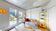 Located at 120 Place Charles-Le Moyne in Longueuil, Quebec, this thoughtfully designed studio offers a clean, contemporary aesthetic across a single level. The open-concept living space features warm light wood flooring, crisp white walls, and a striking exposed concrete ceiling that lends an industrial-modern character to the interior. Large sliding glass doors and oversized windows flood the space with natural light while framing views of the surrounding urban greenery and cityscape, creating an airy and inviting atmosphere.

The living area flows seamlessly into a compact, well-appointed kitchen outfitted with white cabinetry, stainless steel appliances including a refrigerator, oven, and built-in microwave, and a clean white countertop. A wall-mounted split air conditioning unit ensures year-round comfort. A set of sliding closet doors provides convenient storage without compromising the open feel of the space.

The bathroom is finished to a high standard, featuring large-format cream-toned floor tiles, a sleek floating vanity with integrated sink and black hardware, recessed lighting, and white wall surfaces throughout. The result is a calm, spa-like environment that complements the modern tone of the rest of the unit. Overall, this studio delivers a refined and functional urban living experience in a prime Longueuil location.