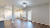 This single-floor unit offers a bright, clean, and functional layout with a cohesive neutral color palette throughout. The open-concept living area greets you at the entry, featuring rich wood-look hard flooring, a ceiling fan with light fixture, and multiple windows dressed with white blinds that allow natural light to fill the space generously. A decorative column adds a subtle architectural detail to the living area, which flows seamlessly toward the kitchen.

The kitchen is a standout feature, equipped with grey shaker-style cabinetry, a white hexagonal tile backsplash, white countertops, and a full suite of stainless steel appliances including a refrigerator, dishwasher, microwave, and range. A central island provides additional workspace and casual seating. Built-in shelving nooks adjacent to the kitchen add practical storage and display options.

The bedrooms are finished with plush carpeting and ceiling fans, with one bedroom offering a large window that brings in ample natural light. The bathroom is clean and well-appointed, featuring a white vanity with brushed nickel hardware, a large mirror, and a full tub-shower combo with tiled surround and wood-look flooring. Track lighting and consistent trim work complete this well-maintained, move-in-ready space.