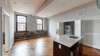 Located in Philadelphia's vibrant Fishtown neighborhood, this single-floor unit masterfully blends industrial heritage with contemporary living. The open-concept living and kitchen area is anchored by rich, original hardwood floors and striking exposed brick walls adorned with large, arched multi-pane windows framed in black—flooding the space with natural light and offering views of the surrounding urban streetscape.

The kitchen is well-appointed with dark mahogany cabinetry, white quartz countertops, a central island with a sink, and a full suite of stainless steel appliances including a refrigerator, electric range, and microwave. A dedicated laundry closet off the main living area houses a stacked Electrolux washer and dryer for added convenience.

The bedroom features plush carpeting, elevated ceilings, and its own exposed brick accent wall with dual black-framed windows, creating a warm yet character-rich retreat. A ceiling fan adds comfort to the space.

Two bathrooms are finished with large-format dark slate tile flooring and tub-shower combinations tiled in matching dark stone, offering a sleek, modern contrast to the unit's industrial aesthetic. Exposed structural beams with conduit detailing throughout the ceiling reinforce the building's converted loft character.