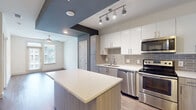 Located at 290 M.L.K. Jr Dr SE in Atlanta, Georgia, this modern single-floor unit offers a well-designed open layout with contemporary finishes throughout. The kitchen serves as a central highlight, featuring a large island with quartz countertops, two-tone cabinetry combining crisp white upper cabinets with wood-grain lower cabinets, a subway tile backsplash, and a full suite of stainless steel appliances including a refrigerator, electric range, over-the-range microwave, and dishwasher. Track lighting and recessed ceiling details add a stylish, modern touch to the kitchen and entry area. The open-plan layout connects the kitchen seamlessly to the living area, which features warm wood-look flooring and a ceiling fan. Bedrooms are carpeted and bathed in natural light from large windows with blinds, providing views of the surrounding community. The bathroom is finished with marble-look tile on both the floors and tub surround, complemented by a soaking tub with shower, a vanity with storage, and access to a walk-in closet with built-in shelving. The overall ambiance is clean, bright, and contemporary, reflecting a move-in-ready aesthetic ideal for modern urban living in Atlanta.