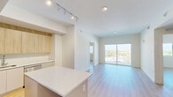 Located at 1715 N Dixie Hwy in Lake Worth Beach, FL, this modern 2-bedroom, 2-bathroom residence offers a thoughtfully designed open-concept layout with clean lines and contemporary finishes throughout. Light wood-tone flooring flows seamlessly across the living areas, complementing the bright, white walls and creating a warm, airy ambiance.

The kitchen is a standout feature, showcasing a large quartz-topped island, two-tone cabinetry with natural wood upper cabinets and white lower cabinets, stainless steel appliances, and track lighting overhead. It opens directly into the combined dining and living area, which is bathed in natural light and leads to a private balcony with open outdoor views.

Both bedrooms are well-proportioned and serene, with the spacious primary bedroom offering generous closet space, including a walk-in closet with wire shelving systems. The secondary bedroom features a sliding closet door for efficient storage. An additional den provides flexible space for a home office or extra living area.

The two bathrooms are finished in a clean, modern style — one featuring a glass-enclosed tiled shower, and the other a full tub-shower combination, both with white vanities and wood-look flooring. A dedicated laundry area and a hallway connecting all rooms complete this well-appointed residence.