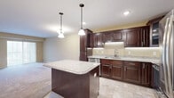 Located at 1411 Adams St in Mankato, MN, this one-bedroom, one-bathroom unit offers a well-designed single-floor layout with a thoughtful mix of finishes and functional spaces. The open-concept kitchen and living area serves as the heart of the unit, anchored by a granite-topped center island illuminated by stylish pendant lights. Rich dark-espresso cabinetry lines the kitchen walls, complemented by granite countertops, tile flooring, and a full suite of stainless steel appliances including a French door refrigerator, range, microwave, and dishwasher. The living area transitions seamlessly from the kitchen, featuring plush carpeting and a sliding glass door that opens to a private balcony, filling the space with natural light. The bedroom is generously sized, offering carpet flooring, a ceiling fan, and a window with outdoor views. A dedicated closet provides ample storage. The bathroom includes a dark-wood vanity with drawers, a tub-shower combination, tile flooring, and grab bars. Additional conveniences include an in-unit laundry area and a utility room. Neutral warm tones throughout create a clean, cohesive ambiance.