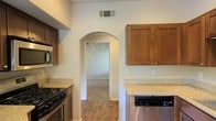 This single-story home offers a well-designed layout that balances functionality and comfort. The kitchen is a standout feature, showcasing warm-toned wood cabinetry that provides generous storage space, complemented by light stone-look countertops that offer ample workspace. Stainless steel appliances, including a gas range, built-in microwave, and dishwasher, add a modern, practical touch to the kitchen's overall aesthetic. A distinctive arched doorway serves as a charming architectural detail, seamlessly connecting the kitchen to the adjacent living space and lending the home a sense of character and flow. The flooring throughout features wood-look planks that bring warmth and continuity across the space. Neutral-toned walls throughout keep the interior feeling bright and open, providing a versatile backdrop for a variety of furnishing styles. The single-floor layout ensures easy accessibility and a cohesive living experience, making the home both practical and inviting. Ceiling vents are thoughtfully integrated to maintain comfortable climate control throughout. Overall, the space presents a clean, move-in-ready environment with classic design elements and modern conveniences.