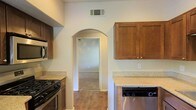 This single-story home offers a well-designed layout that balances functionality and comfort. The kitchen is a standout feature, showcasing warm-toned wood cabinetry that provides generous storage space, complemented by light stone-look countertops that offer ample workspace. Stainless steel appliances, including a gas range, built-in microwave, and dishwasher, add a modern, practical touch to the kitchen's overall aesthetic. A distinctive arched doorway serves as a charming architectural detail, seamlessly connecting the kitchen to the adjacent living space and lending the home a sense of character and flow. The flooring throughout features wood-look planks that bring warmth and continuity across the space. Neutral-toned walls throughout keep the interior feeling bright and open, providing a versatile backdrop for a variety of furnishing styles. The single-floor layout ensures easy accessibility and a cohesive living experience, making the home both practical and inviting. Ceiling vents are thoughtfully integrated to maintain comfortable climate control throughout. Overall, the space presents a clean, move-in-ready environment with classic design elements and modern conveniences.