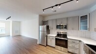 Located at 5324 Hard Scrabble Road in Blythewood, SC, this one-bedroom, one-bathroom unit offers a well-designed single-floor layout with a clean, modern aesthetic throughout. The open-concept kitchen and living area serves as the heart of the home, featuring warm hardwood-style flooring, sleek track lighting, and large windows that invite natural light. The kitchen is outfitted with gray shaker-style cabinetry, white quartz countertops, a classic subway tile backsplash, a stainless steel farmhouse sink, and a full suite of stainless steel appliances, including a refrigerator, range, microwave, and dishwasher. A built-in wine rack adds a thoughtful touch to the cabinetry design. The living area flows naturally from the kitchen, providing a bright and versatile open space. The bedroom is a comfortable retreat finished with plush wall-to-wall carpeting, a ceiling fan, and windows with exterior views. It connects to a generously sized walk-in closet equipped with multi-tiered wire shelving for ample storage. The bathroom features a full tub-shower combination with white tile surround, gray cabinetry for storage, and wood-look flooring, completing this well-appointed home.