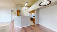 This single-story residence offers a well-organized layout with a variety of functional spaces. The kitchen is designed for efficiency, featuring warm-toned wooden cabinetry, white appliances including a refrigerator, electric range, built-in microwave, and dishwasher. A textured half-wall breakfast bar separates the kitchen from the adjoining living area, which is finished with durable wood-look flooring. Recessed fluorescent lighting illuminates the kitchen, while the elevated ceiling adds a sense of openness to the space.

A dedicated laundry alcove is conveniently accessible off the kitchen, complete with an electrical panel and utility storage. The bedrooms feature plush carpeting and crown molding, with ceiling fans providing added comfort. Large windows allow generous natural light and offer views of the surrounding landscape. One bedroom features hardwood-style flooring and a tall arched window with expansive scenic views.

The bathroom is appointed with a wooden vanity, framed mirror, tiled tub-shower combination, and direct access to a walk-in closet with built-in shelving. Throughout the unit, neutral tones and clean white trim contribute to a cohesive, practical aesthetic.