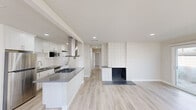 This well-designed single-story home offers 2 bedrooms and 2 bathrooms within a thoughtfully laid-out floor plan. Light wood-style flooring flows consistently throughout, lending a clean, cohesive aesthetic to every room.

The open-concept kitchen and living area forms the heart of the home. The kitchen is outfitted with white shaker cabinetry, gray quartz countertops, a subway tile backsplash, stainless steel appliances including a gas range and refrigerator, a deep single-basin sink, and a central island with a built-in gas cooktop and a statement stainless steel hood. The living area features a striking floor-to-ceiling tiled fireplace, adding a bold architectural focal point. Large sliding glass doors and multiple windows flood the space with natural light and provide outdoor access.

The primary bedroom is generously proportioned, with wide windows that invite ample daylight. The second bedroom is cozy and bright, also benefiting from natural light. A dedicated closet provides convenient storage.

Both bathrooms are finished with white cabinetry and neutral countertops. One bathroom includes a stand-alone shower stall with built-in shelving. The overall palette of warm whites, soft beiges, and light wood tones creates a bright, airy, and move-in-ready atmosphere throughout the home.