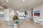 Located at 624 NE 2nd St in Dania Beach, Florida, this single-story amenity facility offers a thoughtfully designed and well-appointed interior spread across a spacious single level. Light wood-look flooring flows throughout, unifying the distinct functional zones and contributing to the space's clean, contemporary aesthetic.

The welcoming lounge area serves as the heart of the space, featuring a striking circular sectional sofa in white and blue, set atop a striped area rug. Bold, colorful abstract artwork adorns the walls alongside a wall-mounted flat-screen TV and a sleek navy blue credenza with gold accents. Tall tropical plants, sheer draping curtains, and glass-top accent tables complete the sophisticated yet inviting atmosphere. Floor-to-ceiling glass doors open to an outdoor patio, bathing the interior in abundant natural light and providing views of the surrounding landscape.

The fitness center is generously sized and fully equipped, featuring cardio machines including treadmills and a stair climber, strength-training stations, a full rack of dumbbells, workout benches, and a dedicated functional training area with stability balls and resistance equipment. Floor-to-ceiling mirrors amplify the sense of space, while multiple windows ensure bright, naturally lit workouts.

A clean, ADA-accessible corridor leads to restrooms and utility closets, rounding out this well-organized, modern facility.