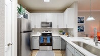 This single-floor residence offers a thoughtfully designed layout that balances comfort and modern functionality across its key living spaces. The kitchen is a standout feature, showcasing two-tone cabinetry with crisp white upper cabinets and soft grey lower cabinets, complemented by white quartz countertops and a neutral subway tile backsplash. A full suite of stainless steel appliances — including a refrigerator, electric range, built-in microwave, and dishwasher — equips the space for everyday cooking. A skylight overhead fills the kitchen with natural light, while light wood-look flooring adds warmth underfoot. The living area is bright and welcoming, featuring crown molding, a ceiling fan, and French doors that open to an outdoor area, allowing natural light to flow freely into the room. The bedroom is carpeted for comfort and includes a ceiling fan, a window overlooking greenery, and built-in shelving with a compact desk nook, providing practical storage and workspace. An in-unit washer and dryer is accessible from the bedroom hallway. The bathroom is finished with tile-surround tub and shower combination, wood-look flooring, and neutral wall tones, creating a clean and functional space throughout.