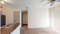 This single-floor residential unit offers a practical and comfortable layout designed for everyday living. The kitchen is a standout feature, equipped with rich wood-toned cabinetry, a full suite of black appliances including an electric range, over-the-range microwave, and a full-size refrigerator, complemented by hardwood-style flooring and a double stainless steel sink set into a laminate countertop. A bold yellow accent wall adds a touch of warmth and character to the cooking space.

The living area transitions seamlessly from the kitchen, featuring neutral wall-to-wall carpeting and clean white walls that create a bright, open atmosphere. A hallway connects the main living space to the private areas of the unit, maintaining a clear and logical flow throughout.

The bedroom is generously sized with soft carpeting underfoot, a ceiling fan with a light fixture for year-round comfort, and a large sliding glass door dressed with vertical blinds that allows natural light to filter in. An additional carpeted room with a window and ceiling fan offers flexibility as a second bedroom or office.

The bathroom is efficiently designed with a single-sink vanity featuring white cabinetry, a well-lit mirror, hardwood-style flooring, and a full tub-shower combination, rounding out this functional and inviting space.