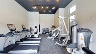 This well-appointed fitness center offers a comprehensive workout environment designed to support a variety of exercise routines. The space is anchored by a row of True-brand treadmills and a stationary bike, providing dedicated cardio options for residents or users. A multi-station cable and strength machine occupies the central area, offering versatile resistance training capabilities, while a freestanding dumbbell rack stocked with a full range of weights supports free weight workouts.

The interior design strikes a bold contrast between the crisp white walls and the deep navy-painted ceiling, which is fitted with industrial-style track lighting that provides focused, warm illumination throughout the space. Durable patterned carpet tile covers the floor, lending texture and resilience suited for a high-traffic fitness environment. A large window along one wall introduces natural light and a view of the outdoors, creating an open and motivating atmosphere. The overall layout is efficiently organized, maximizing usable floor space while keeping equipment accessible. The combination of modern finishes and thoughtfully arranged equipment gives the fitness center a clean, professional character.