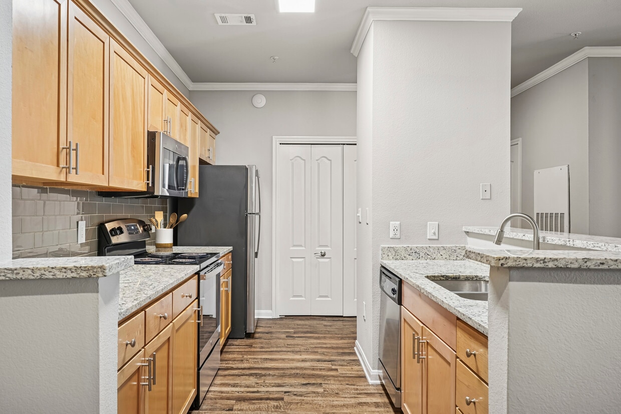 Kitchen with oak cabinetry, speckled granite countertops, stainless steel appliances, and hard surface flooring - eaves Twin Creeks