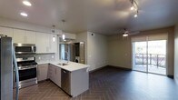 This single-floor space showcases a thoughtfully designed open-concept layout that connects the kitchen and living areas for a spacious, cohesive feel. The kitchen is a standout feature, equipped with sleek white cabinetry, a white quartz countertop island with an integrated sink, a stainless steel dishwasher, and a contemporary tile backsplash. Pendant lighting hangs above the island, adding both task illumination and a modern aesthetic touch. Track lighting complements the kitchen area, ensuring the space is well-lit throughout.

The flooring throughout is a striking herringbone-patterned tile that adds visual depth and a refined character to the space. The open living area is bright and versatile, featuring a ceiling fan, neutral walls, and a door that leads to an outdoor area, allowing natural light to flow in. Recessed and accessible laundry units are conveniently tucked within a dedicated nook, adding practical functionality. The overall ambiance is clean, modern, and move-in ready, with a neutral color palette that makes the space feel both welcoming and adaptable.