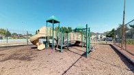 Located at 5280 Tamarack Cir E in Columbus, Ohio, this outdoor recreational space centers around a well-equipped playground designed for active play. The multi-level play structure is finished in green and tan tones, featuring a distinctive curved slide, elevated platforms, a connecting bridge with safety railings, and multiple climbing access points. The structure's pyramid-style canopy rooftops provide a visually appealing design while offering partial shade over the platforms. The play area is surfaced with wood chip mulch, providing a safety-conscious ground cover beneath and around the equipment. The open layout allows for clear sightlines across the entire play zone, making supervision straightforward. A swimming pool is visible adjacent to the playground, suggesting this space is part of a broader community amenity area. The surrounding landscape includes mature trees and open greenery, contributing to a pleasant, park-like atmosphere. The space benefits from abundant natural light under open skies, and its ground-level, single-floor layout ensures easy accessibility for children of various ages. Overall, this outdoor space offers a functional and inviting environment for recreation within the community.