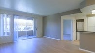 This single-floor residence offers a straightforward and functional layout with a clean, contemporary finish throughout. The main living area is a standout feature, showcasing light-toned hardwood-style flooring that runs seamlessly across the space, lending a sense of warmth and continuity. Neutral gray walls provide a versatile backdrop, complementing the crisp white baseboards and trim that frame the room with a polished look.

A large sliding glass door floods the living area with abundant natural light, creating a bright and welcoming atmosphere. The door opens to an outdoor space, extending the living area and offering a connection to the exterior environment.

An open doorway visible from the main living area leads to an adjoining room, finished with light-toned carpeting, offering a softer, quieter space likely suited for a bedroom or additional living area. The transition between the two spaces is smooth and well-defined, guided by clean white door framing.

Overall, the space presents a well-maintained, move-in ready environment with a minimalist aesthetic. The neutral color scheme, ample natural light, and cohesive flooring choices combine to create a comfortable and adaptable living environment suitable for a variety of furnishing styles and personal tastes.