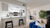 Located at 8546 N 59th Ave in Glendale, Arizona, this single-story, one-bedroom, one-bathroom residence offers a thoughtfully designed layout that maximizes every square foot. The open-concept living and dining area serves as the heart of the home, featuring light-toned tile flooring, bright white walls, and windows dressed with sheer curtains that invite natural light. The kitchen is a standout feature, equipped with stainless steel appliances including a refrigerator, range, and built-in microwave, complemented by crisp white cabinetry, a gray tile backsplash, granite countertops, and a peninsula with bar seating — ideal for casual dining or entertaining. A smart thermostat is conveniently mounted near the kitchen entrance. The bedroom offers a comfortable, well-proportioned retreat with a window providing natural light, tile flooring, and ample closet storage — with three closets found throughout the home. The full bathroom is finished with a granite-topped vanity, white cabinetry, a large mirror, and a shower-tub combination. A hallway connects the living spaces to the private areas of the home, completing this clean and cohesive single-floor layout.