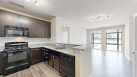 This single-floor residence offers a thoughtfully designed layout that balances style and functionality. The open-concept kitchen is a standout feature, showcasing rich dark espresso cabinetry, granite-style countertops, a subway tile backsplash, and a full suite of black appliances including a refrigerator, gas range, microwave, and dishwasher. A peninsula with an undermount sink connects the kitchen to the living area, creating a seamless flow ideal for entertaining. The living area is finished with light wood-style flooring and is bathed in natural light from large floor-to-ceiling windows that frame views of the surrounding environment. Track lighting adds a modern touch overhead. The bedrooms are carpeted and generously sized, each featuring large windows that bring in abundant natural light. One bedroom includes a ceiling fan for added comfort. The bathroom is finished with tile flooring, a dark vanity consistent with the kitchen cabinetry, and a full soaking tub with tile surround. A spacious walk-in closet with wire shelving and hanging rods provides excellent storage capacity. Throughout the residence, neutral warm tones on the walls complement the light flooring, creating a clean, contemporary ambiance.