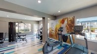 This fitness center is a thoughtfully designed, single-floor space that offers a comprehensive workout environment for users of all fitness levels. The interior is anchored by a striking geometric-patterned floor in shades of blue, gray, and cream, which adds a dynamic, energetic feel to the space and visually defines different workout zones throughout the room.

The cardio area is well-appointed with multiple treadmills, elliptical trainers, and a stair climber, positioned near a window that offers views of an outdoor pool area, providing natural light and a motivating backdrop during workouts. A large, vibrant motivational wall mural of an athlete in motion further energizes this section of the gym.

The strength training area features a multi-station cable machine and a dedicated free weights section with a full rack of dumbbells and an adjustable bench, offering a wide range of resistance training options. The open floor plan, supported by structural columns, allows for generous circulation between equipment stations.

The walls are finished in a warm neutral gray tone, complemented by recessed lighting throughout that ensures consistent, well-distributed illumination. Windows along the perimeter allow natural light to filter in, contributing to a bright and welcoming atmosphere. The space is accessible via a clearly marked entry door and maintains a clean, organized layout that supports an efficient and focused fitness experience.