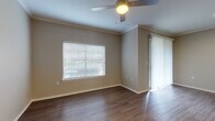 This single-floor residence offers a cohesive and functional layout finished with warm wood-look flooring that flows consistently throughout every room. The open living area is bright and welcoming, featuring crown molding, a ceiling fan with light fixture, and access to an outdoor area via a sliding glass door dressed with vertical blinds. Natural light filters in through horizontal blinds on the windows, lending a comfortable ambiance to the space.

The kitchen is well-equipped for everyday living, outfitted with dark espresso cabinetry, white countertops, a subway tile backsplash, and a full suite of stainless steel appliances including a refrigerator, range, microwave, and dishwasher. Conveniently adjacent to the kitchen is a dedicated laundry area housing a full-size washer and dryer alongside a water heater, keeping all utilities neatly contained.

The bedroom is generously sized, also featuring a ceiling fan and natural light from a window. It includes access to a walk-in closet with built-in wire shelving, offering ample storage. The bathroom is clean and simply appointed, with a tiled tub-shower combination, brushed nickel fixtures, and a toilet, maintaining the neutral, modern palette found throughout the home. The overall design is understated and move-in ready.
